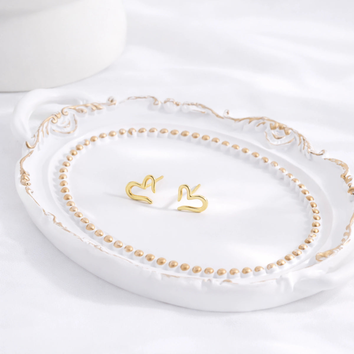 Gold-tone open heart stud earrings displayed on a decorative white tray