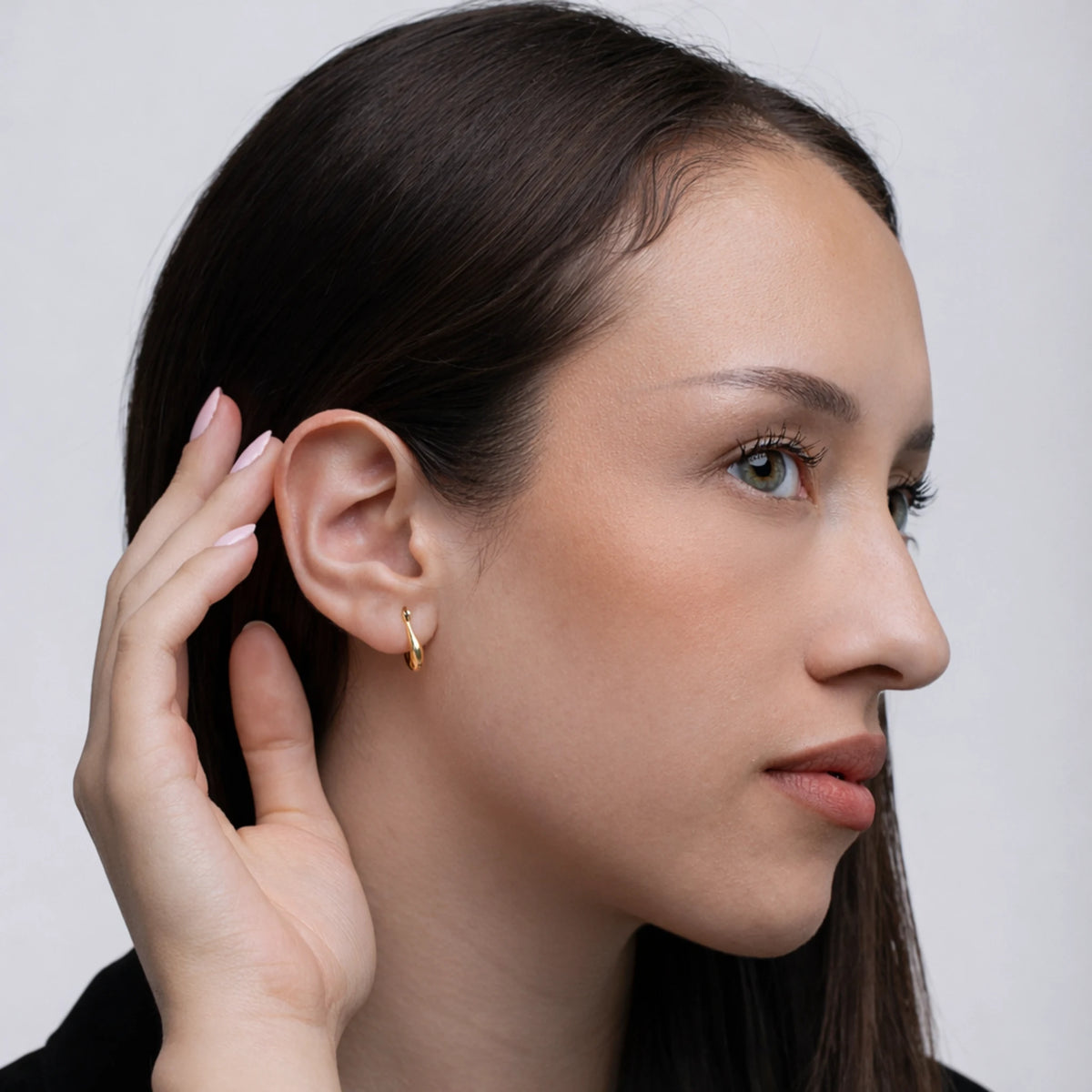 Woman wearing a gold hoop earring with a neutral background