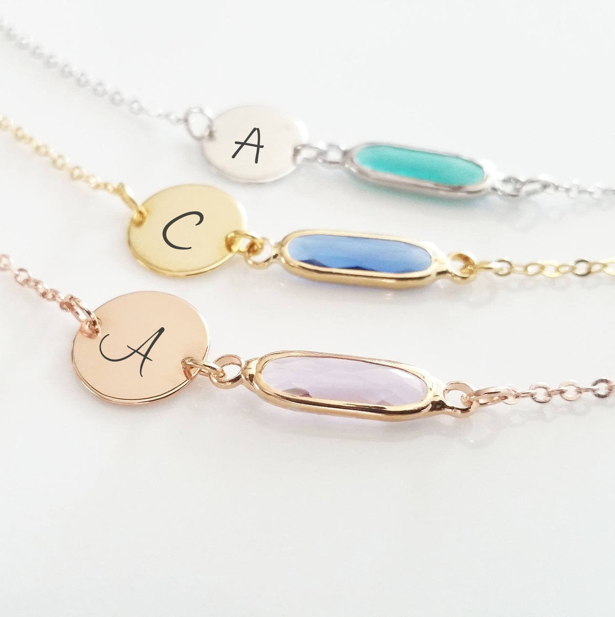 Three bracelets in silver, gold, and rose-gold tones with engraved A, C, and A discs and turquoise, blue, and pale pink elongated stones