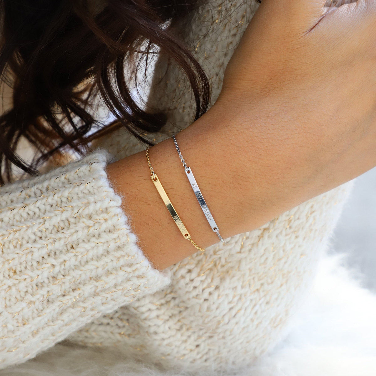 Gold-tone and silver-tone engraved name bar bracelets worn together on a wrist