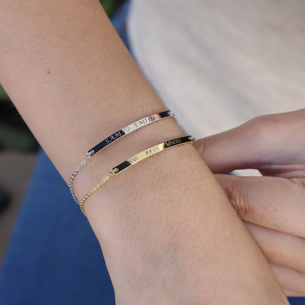 Silver-tone and gold-tone engraved bar bracelets with Roman numerals worn together on a wrist