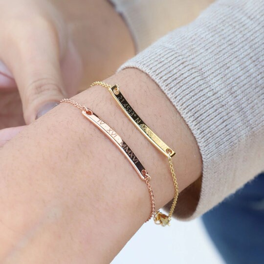 Rose-gold-tone and gold-tone engraved bar bracelets worn together on a wrist beside a light knit sleeve