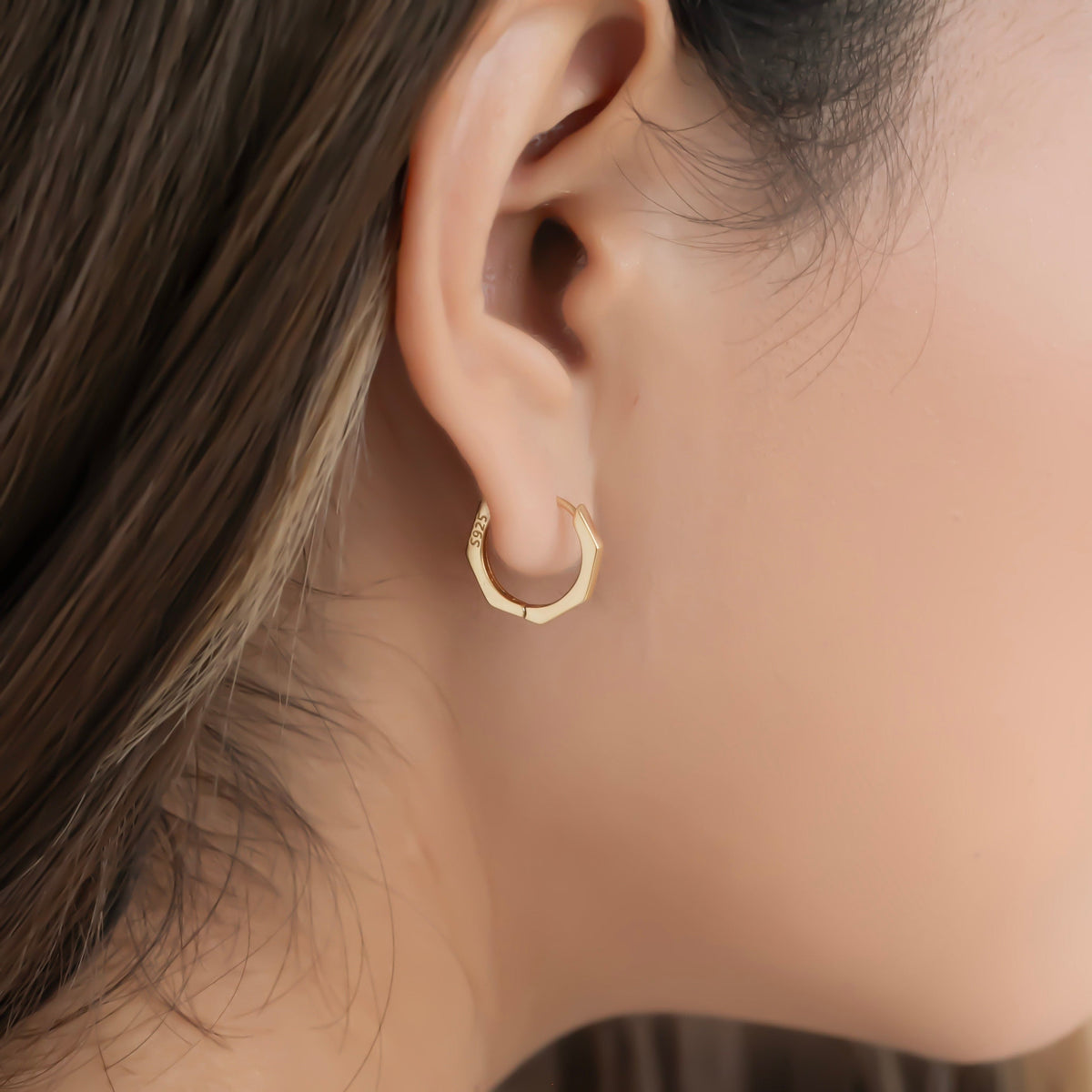 A close-up image of a person wearing a small hoop earring in their left ear.