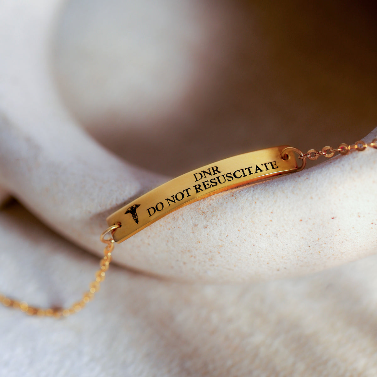 Gold-tone medical ID bar bracelet engraved DNR DO NOT RESUSCITATE on a light fabric surface