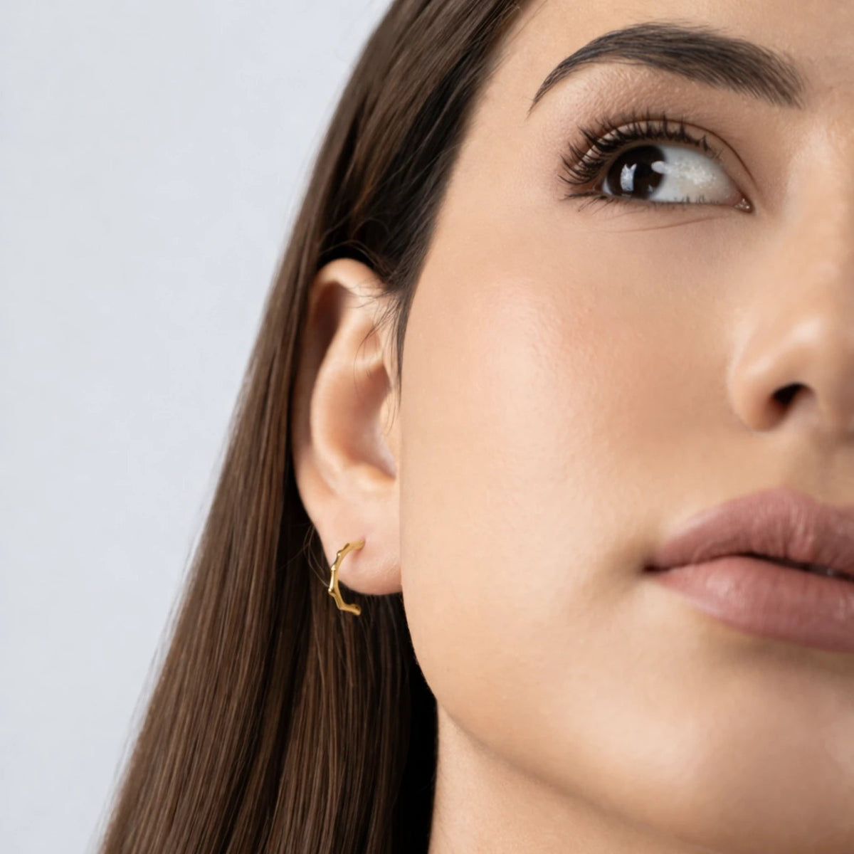 Close-up of a woman wearing a gold earring against a light background