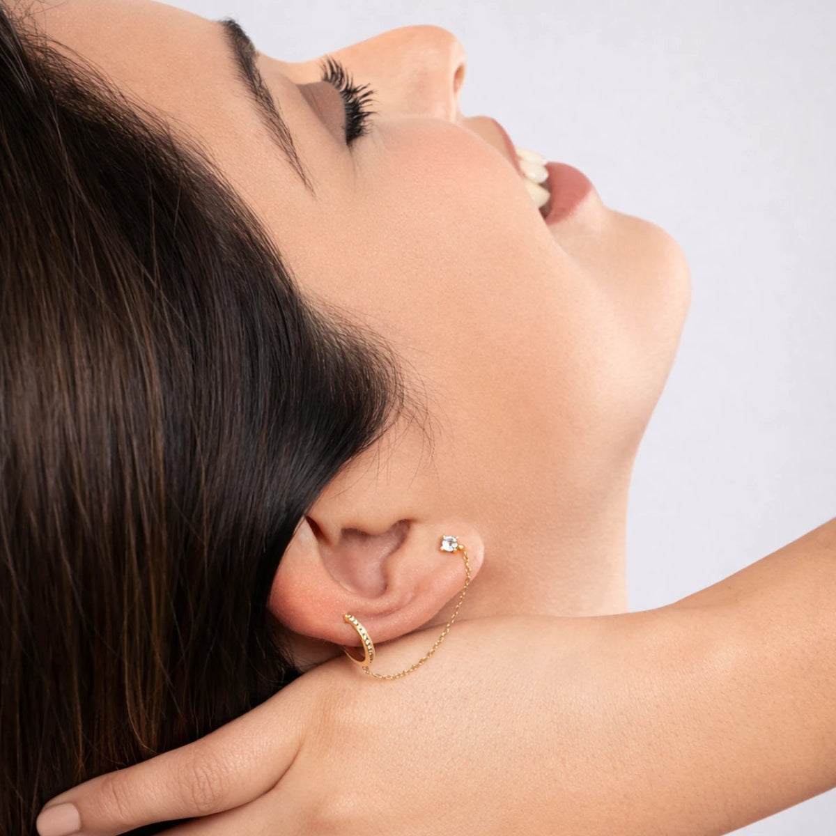 Close-up of a woman adjusting an earring with a plain background