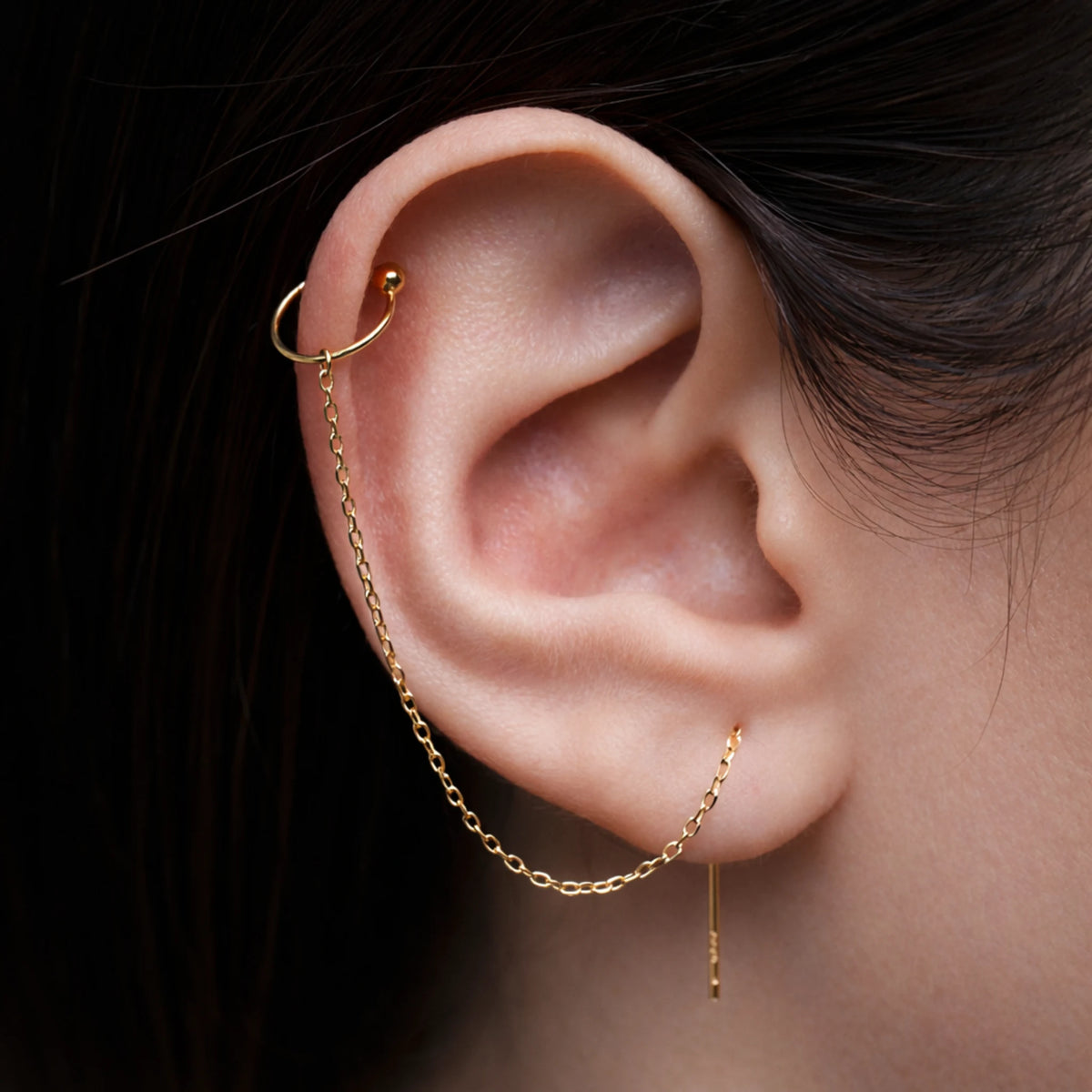Gold ear cuff with chain detail worn by a person