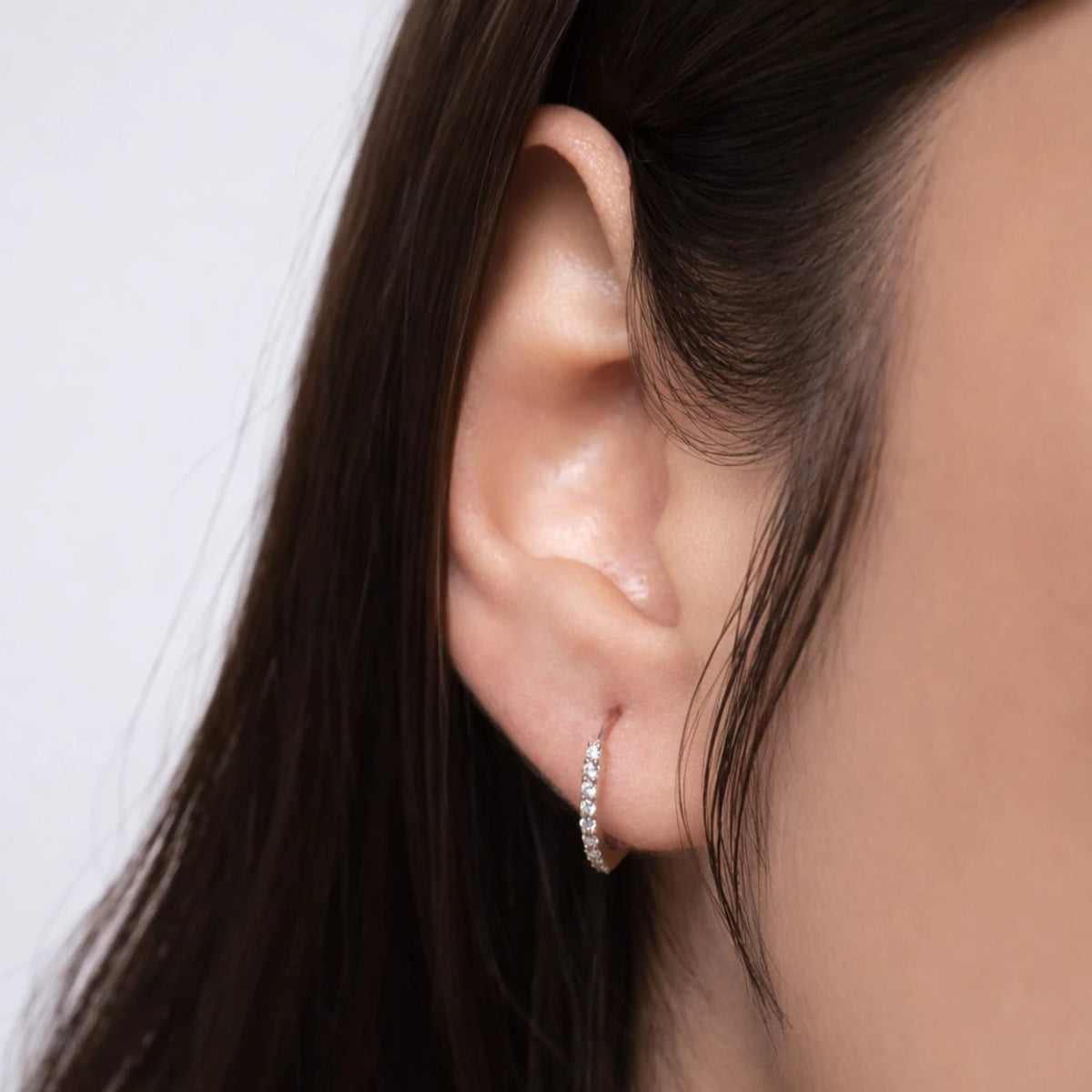 Close-up of a person wearing a diamond earring with a neutral background