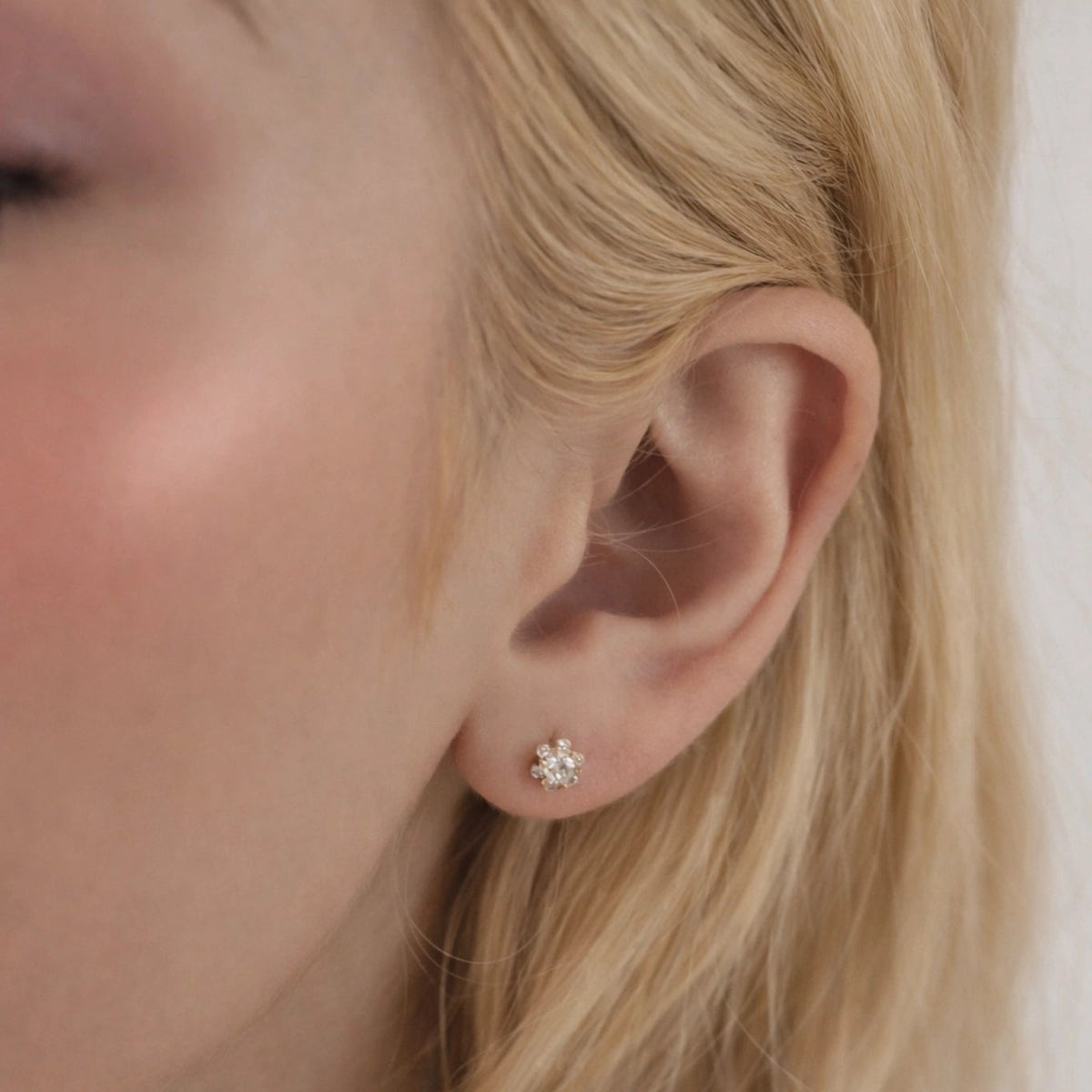 Close-up of a person wearing a diamond stud earring with a blurred background