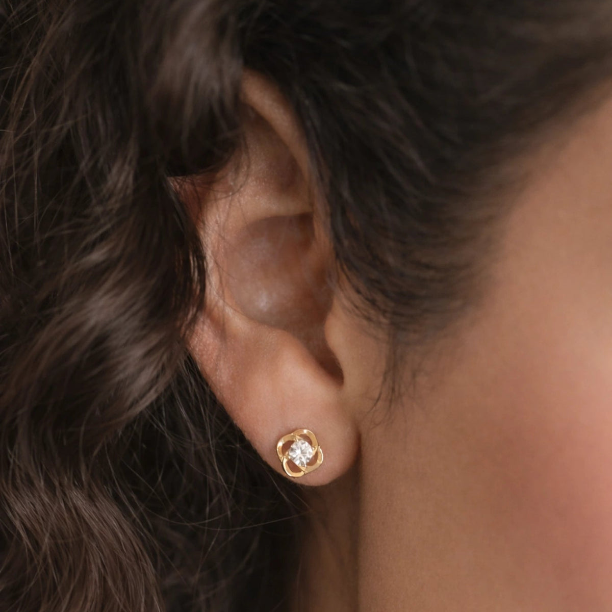 Close-up of an ear wearing a gold earring with a diamond.