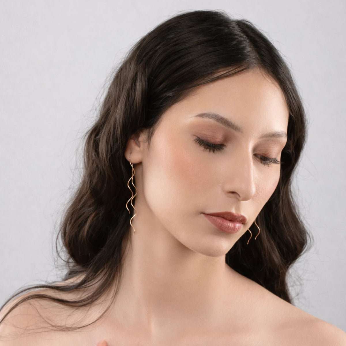 Woman with long dark hair wearing a strapless brown top against a light gray background