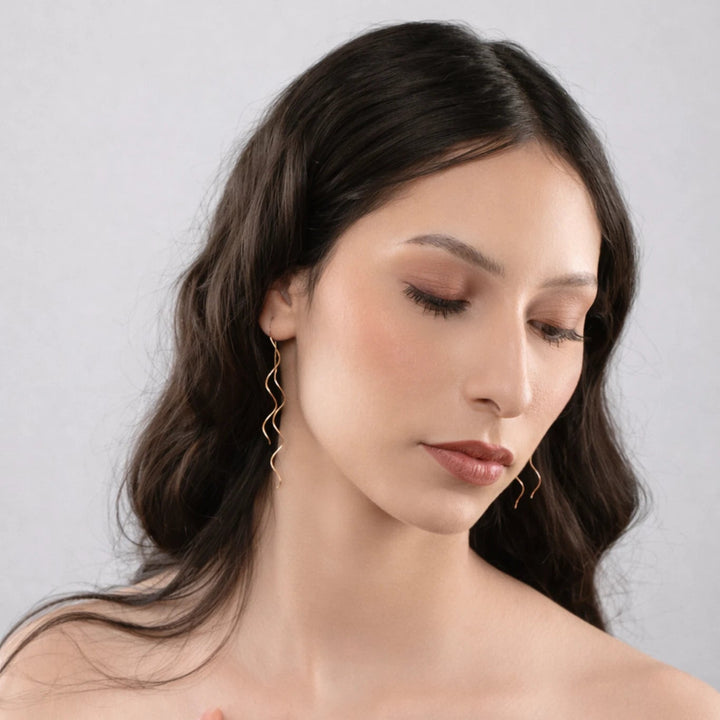 Woman with long dark hair wearing a strapless brown top against a light gray background