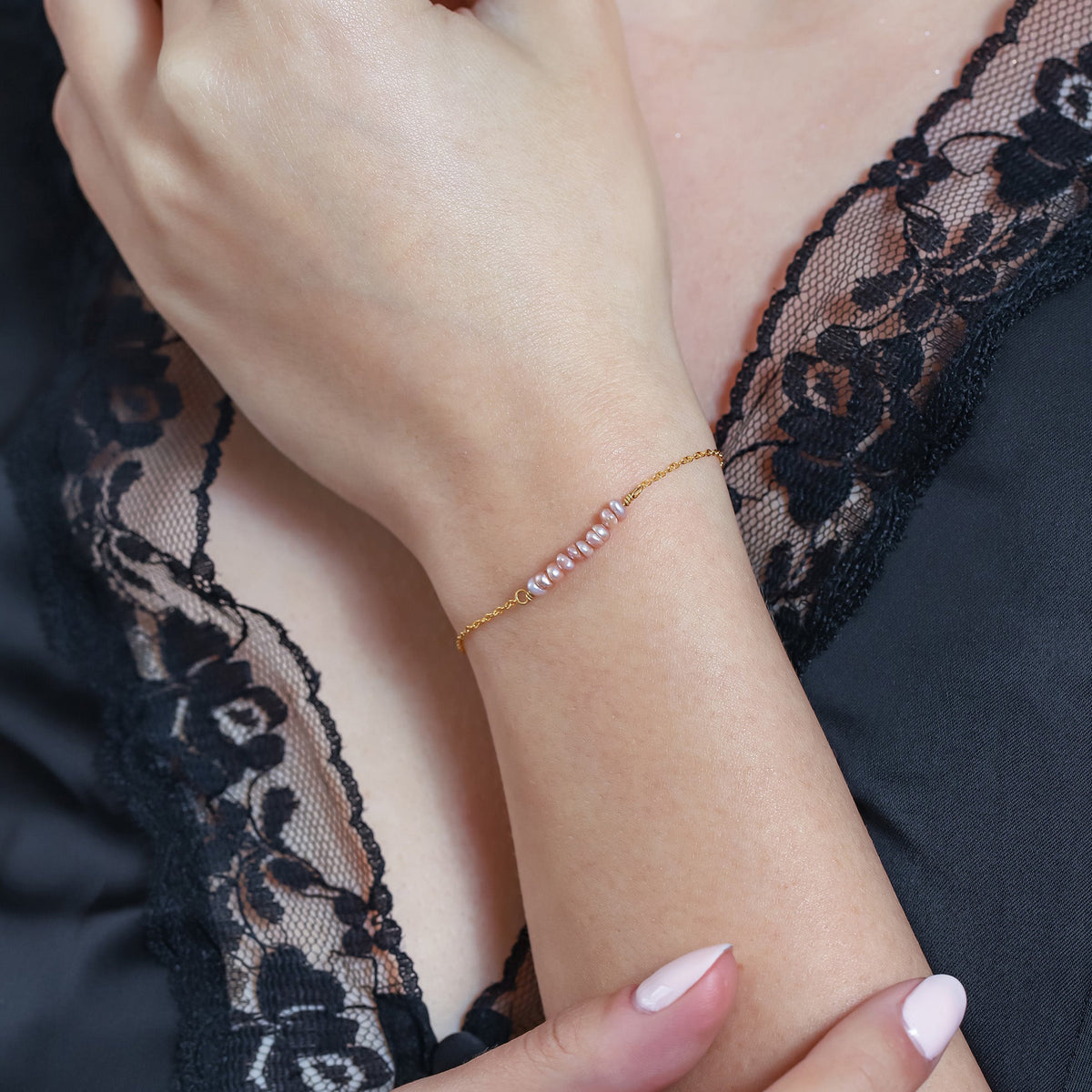 Gold-tone chain bracelet with a row of small purple oval small pearls worn on a wrist