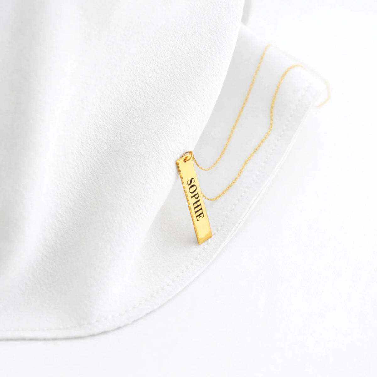 Gold-tone vertical bar necklace engraved with SOPHIE, displayed on a white jewelry stand