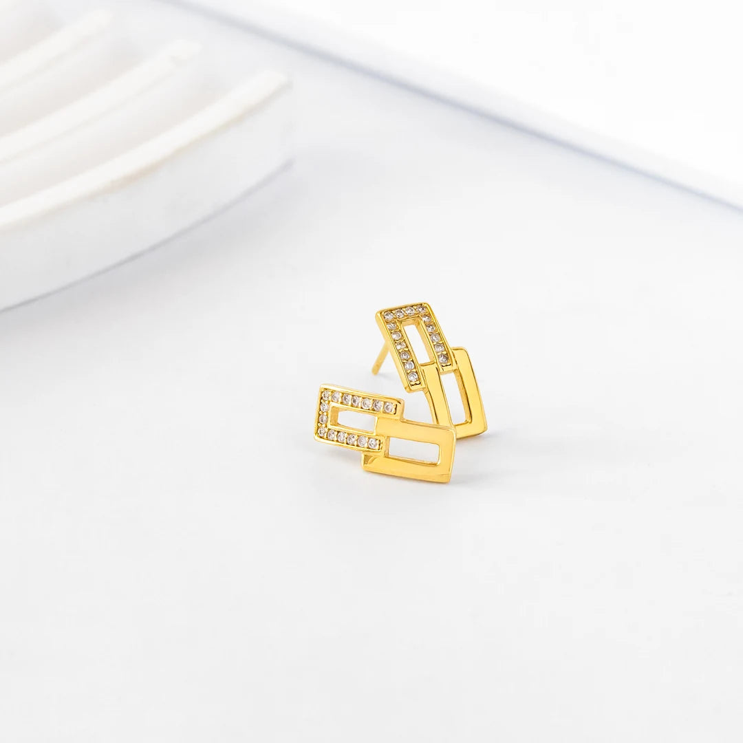 Gold-tone geometric stud earrings with clear stones displayed on a white surface