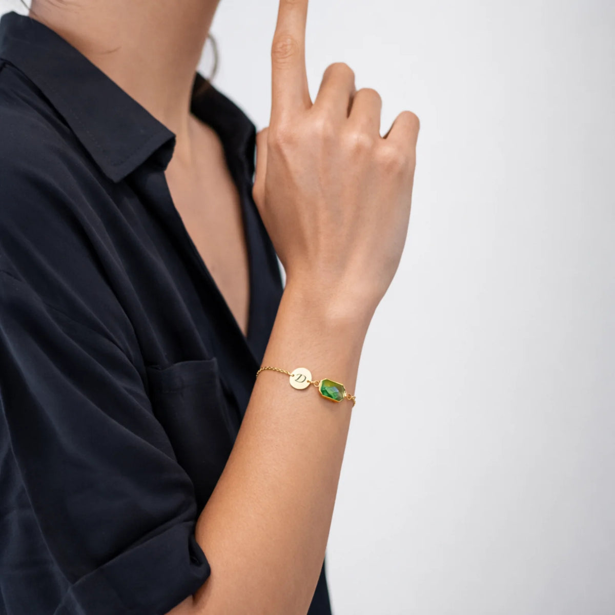 Gold-tone bracelet with engraved D initial disc and green faceted stone worn on a wrist