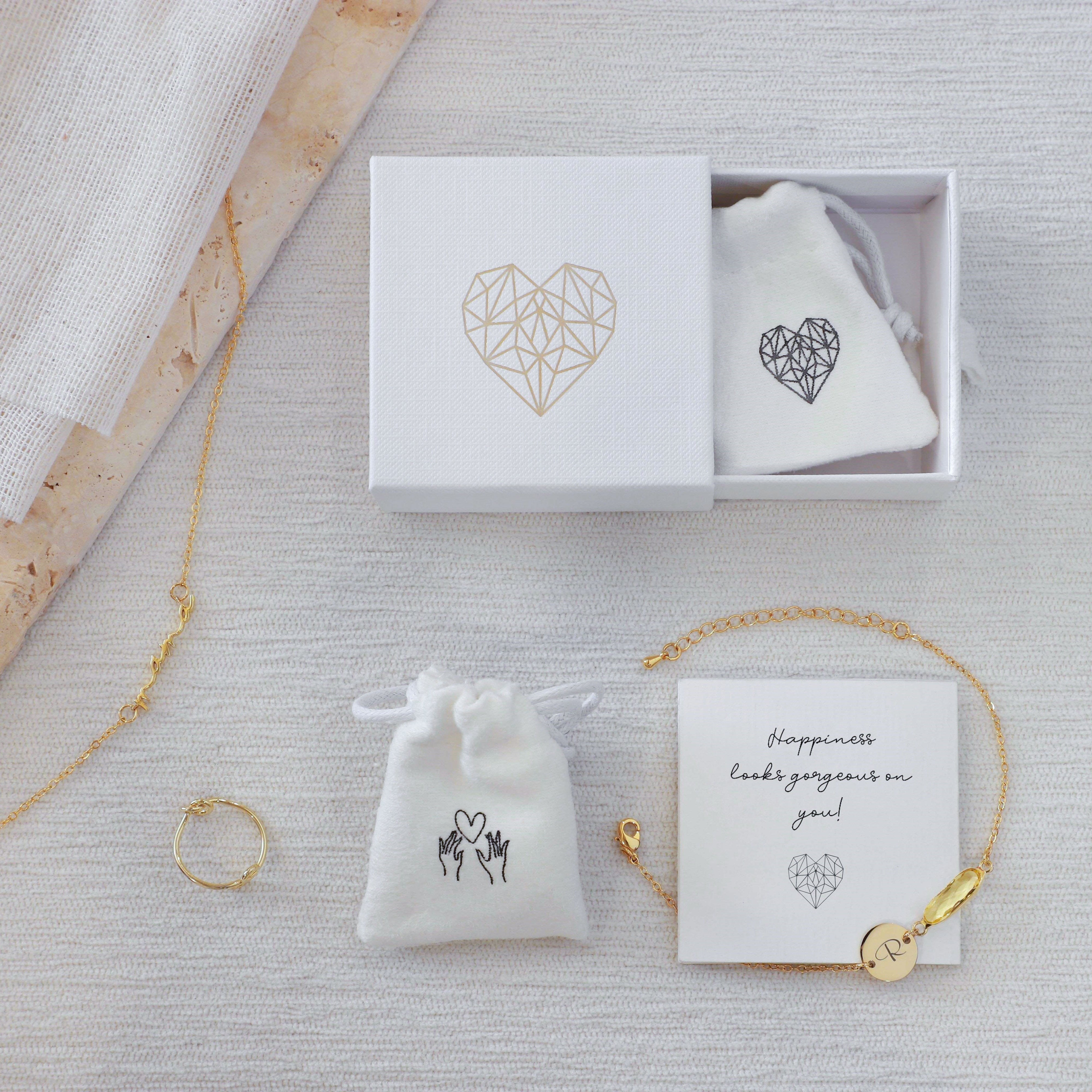 Gold jewelry including a necklace, bracelet, and ring on a textured surface with branded jewelry boxes.