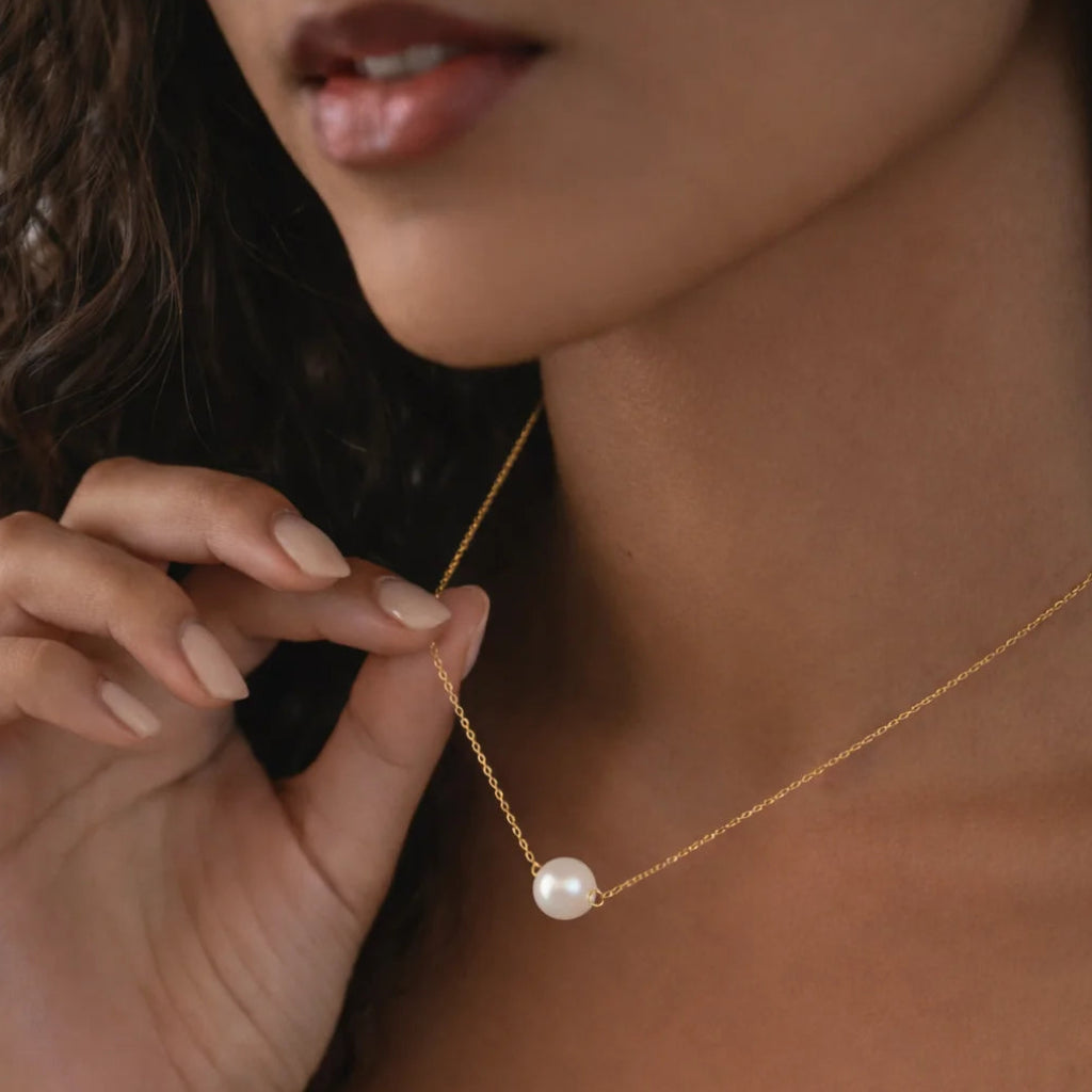 Close-up of a pearl necklace being adjusted by a hand against a blurred background