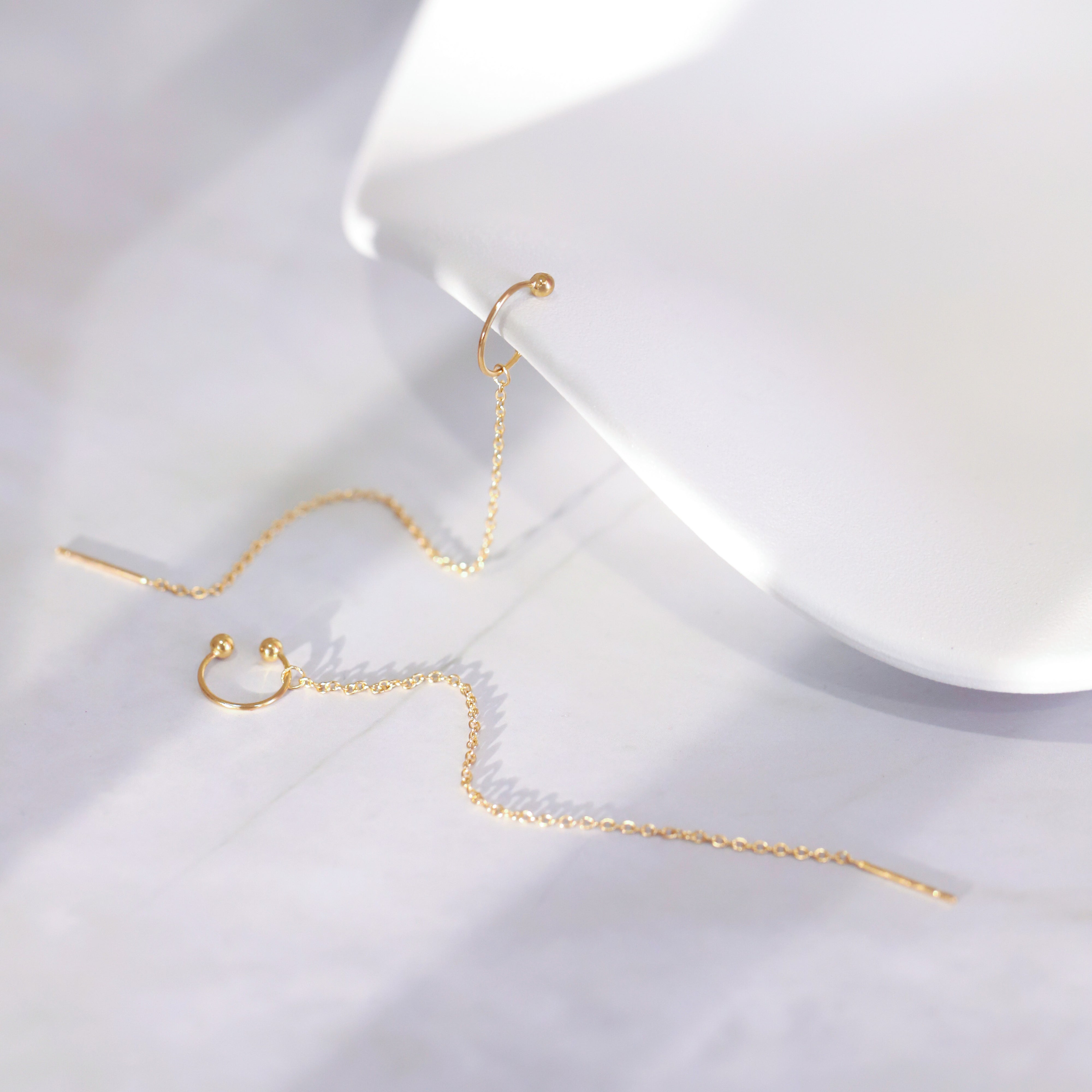 Gold chain earrings on a white surface with a white box in the background