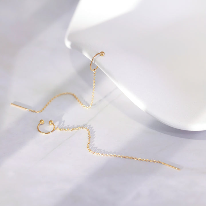 Gold chain earrings on a white surface with a white box in the background