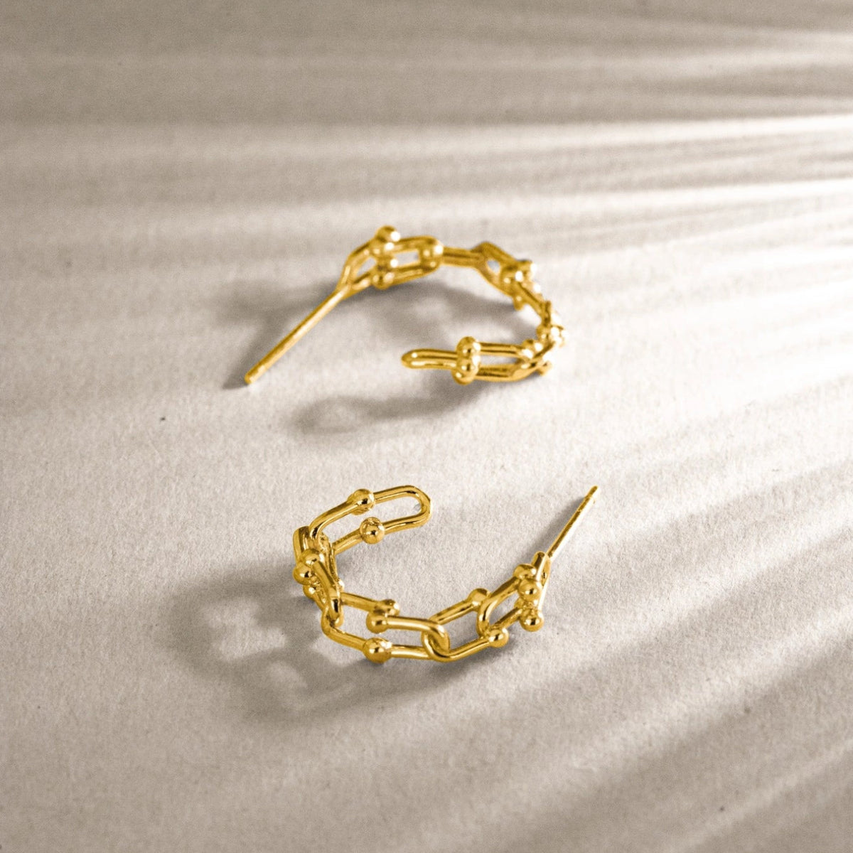 Gold-tone chain link huggie earrings displayed on soft beige fabric