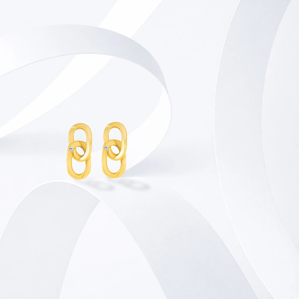 Gold-tone geometric dangle stud earrings with clear stone accents displayed on white sculptural forms