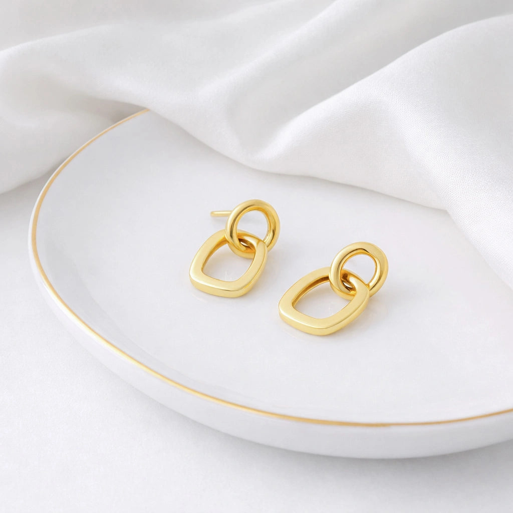 Gold-tone linked stud earrings displayed on a white dish with white fabric