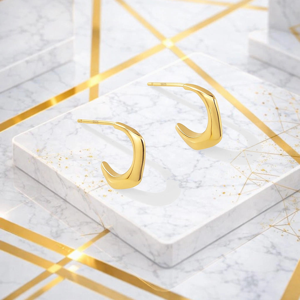 Gold-tone angular hook earrings displayed on a white marble surface with gold accents