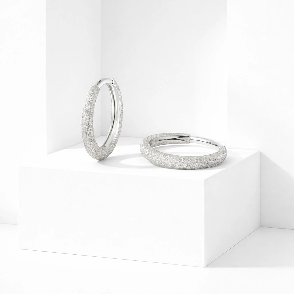 Silver-tone textured hoop earrings displayed on white geometric blocks