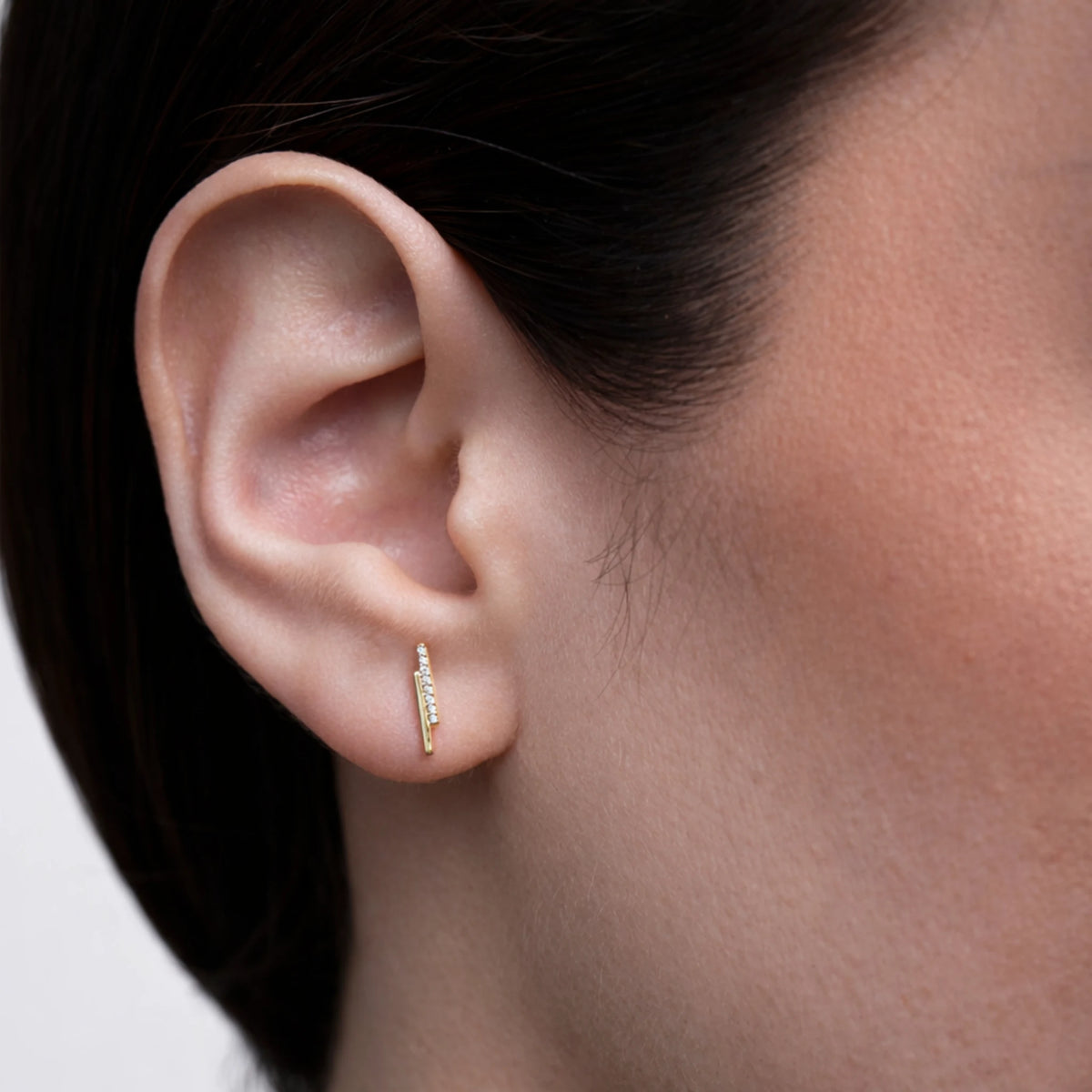 Close-up of an ear wearing a gold earring with a blurred background