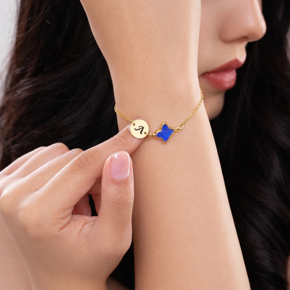 Gold-tone bracelet with engraved A initial disc and blue four-lobed stone worn on a wrist