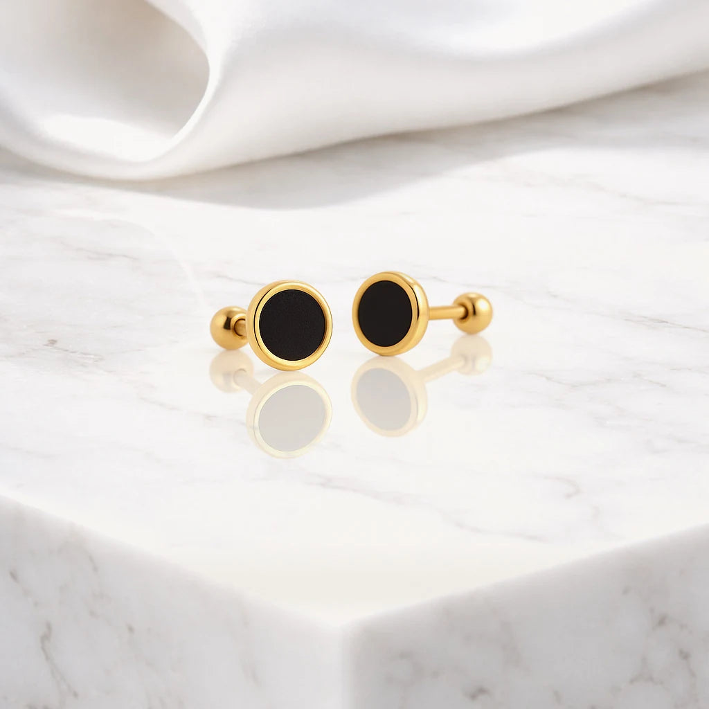 Gold-tone round black stud earrings displayed on a pale marble surface