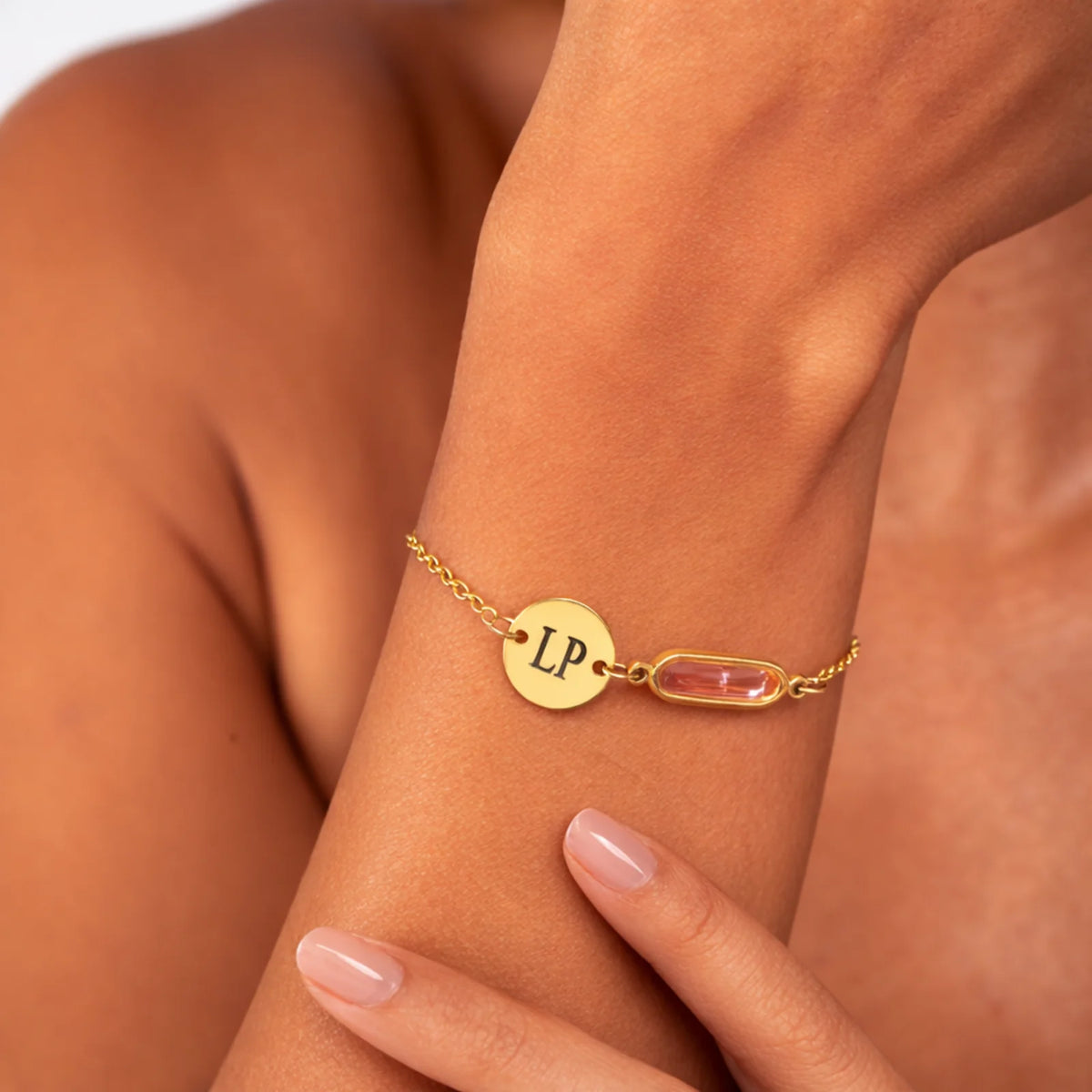 Gold-tone bracelet with engraved LP disc and pale pink rectangular stone worn on a wrist