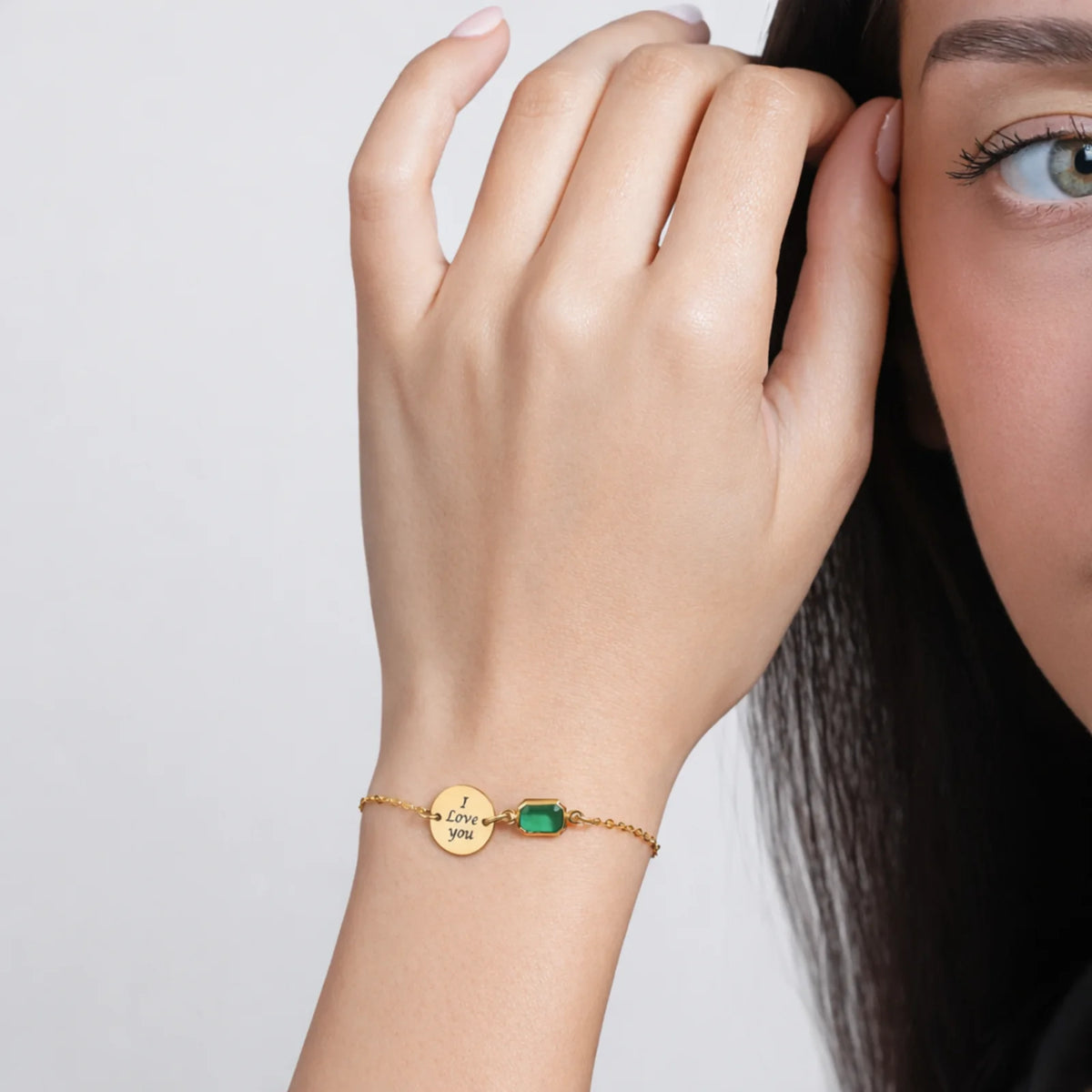 Gold-tone bracelet with round disc engraved I Love You and green rectangular stone worn on a wrist