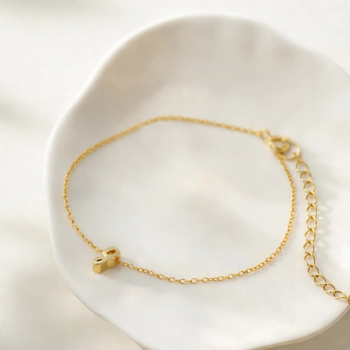 Delicate gold-tone chain bracelet with small cursive g charm and adjustable extender on a white dish