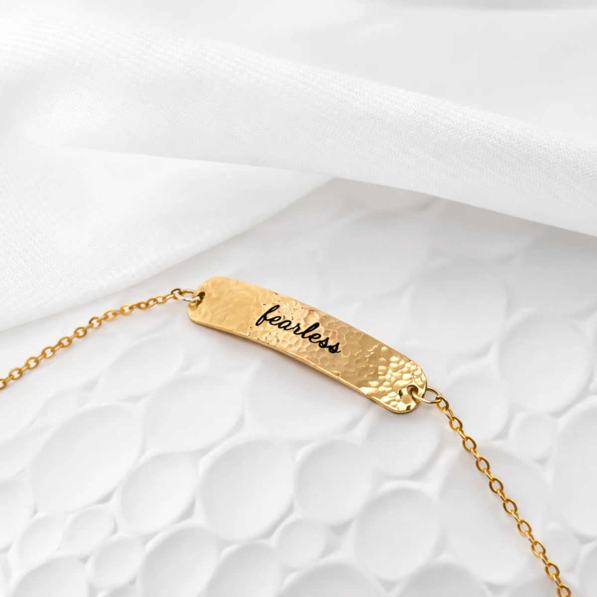 Gold-tone hammered bar bracelet engraved fearless on a textured white surface