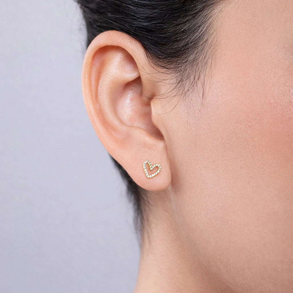 Gold-tone open heart stud earring with clear stones worn on the ear against a light background