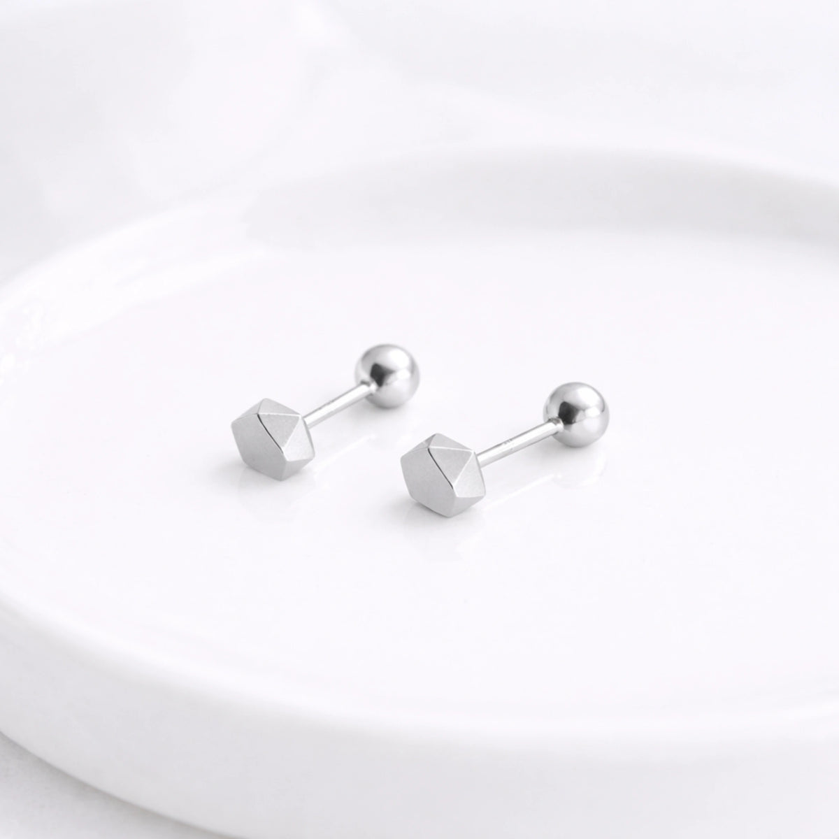 Silver-tone faceted hexagon stud earrings with ball backs displayed on a white surface