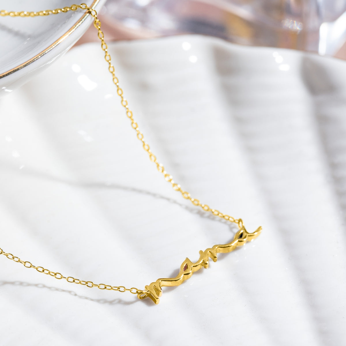 Gold-tone mama script necklace displayed on a glossy white surface