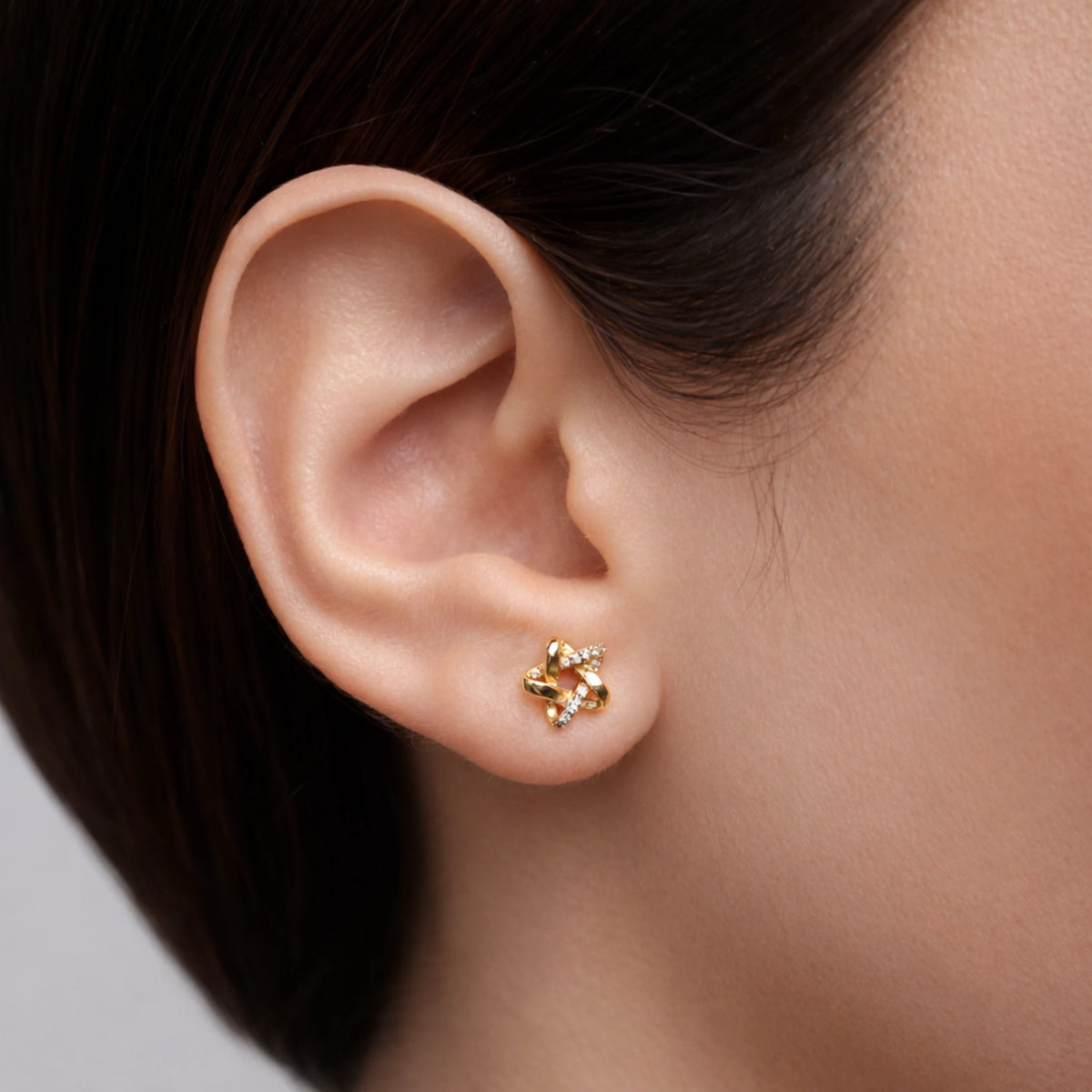 Gold earring worn on a person's ear with a neutral background
