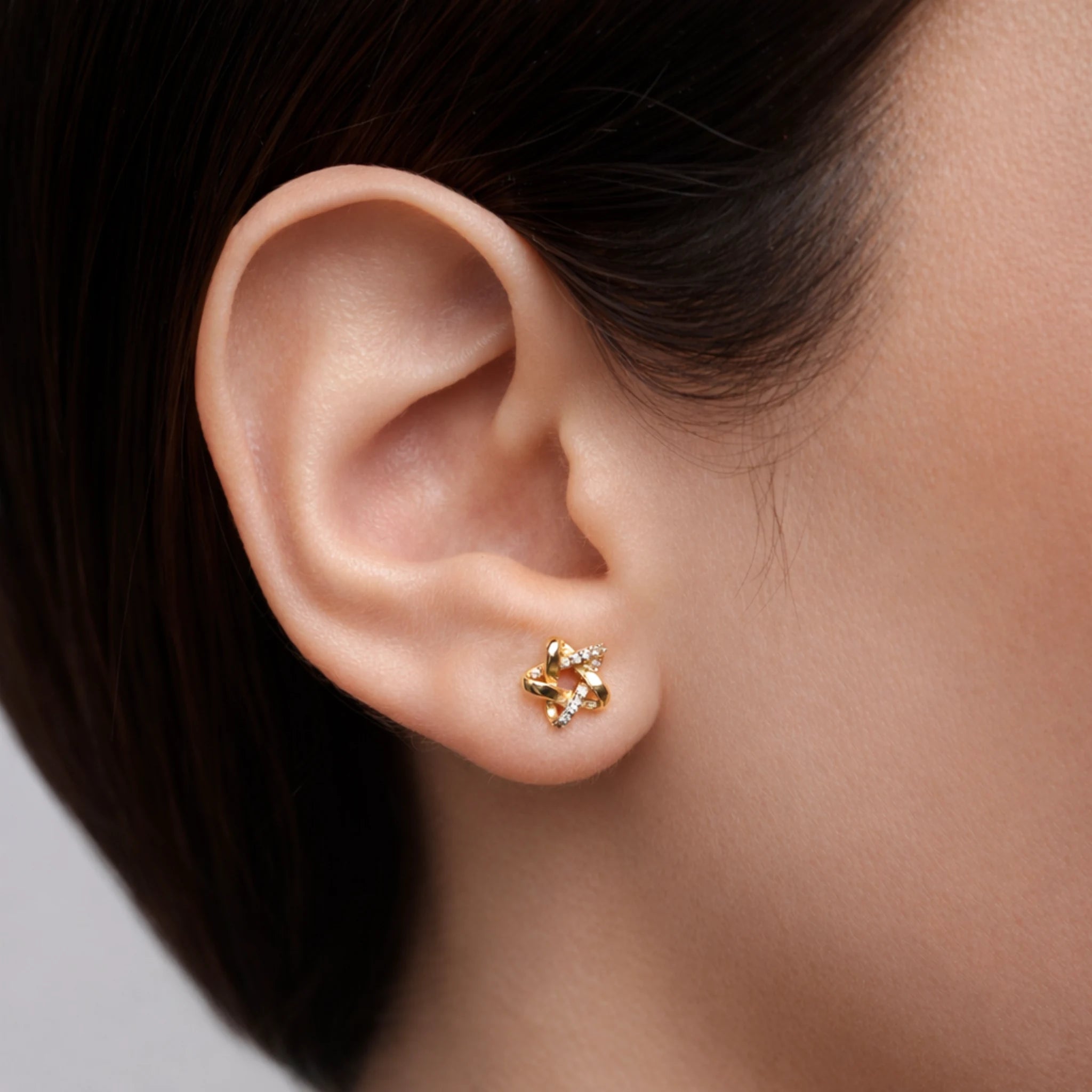 Gold earring worn on a person's ear with a neutral background