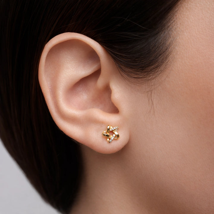 Gold earring worn on a person's ear with a neutral background