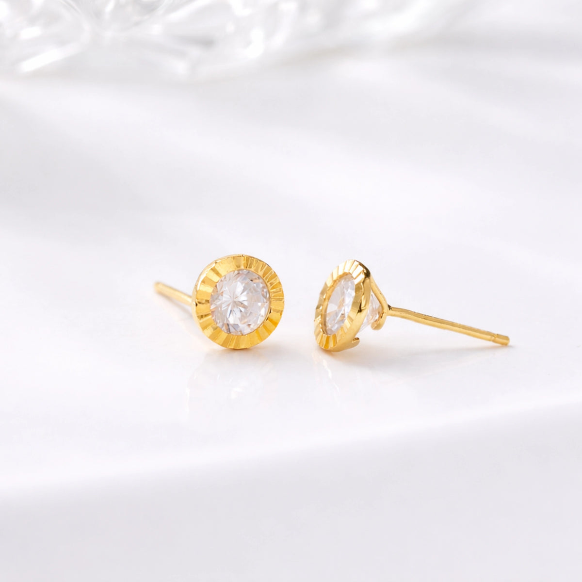 Gold-tone round stud earrings with clear center stones displayed on white fabric