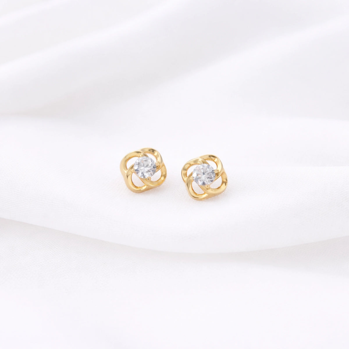 Gold-tone flower stud earrings with clear center stones displayed on white fabric